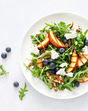 Peach, blueberry and arugula fresh fruit salad with cheese and almond nuts, top view